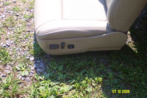 1992 Ford Bronco - Close-up of car seat controls on a tan leather seat, resting on grass and gravel.