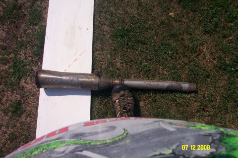 1992 Ford Bronco - Exhaust pipe with "III" logo on white board next to grass. A foot is visible near the pipe.