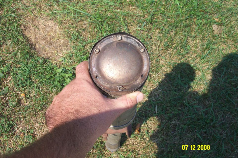 Hand holding an exhaust muffler with a metal cap secured by screws