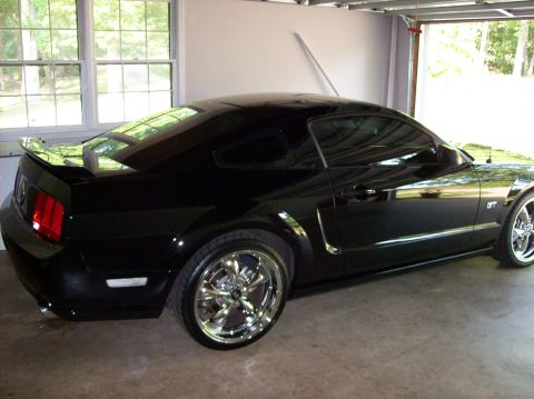 2007 Ford Mustang - A black 2007 Ford Mustang GT coupe is shown from a three-quarter front view, parked inside a garage with custom chrome wheels.