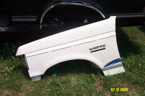 1992 Ford Bronco - White Ford Bronco fender with blue stripe and 'BRONCO' badge. Part of a black vehicle is visible behind it.