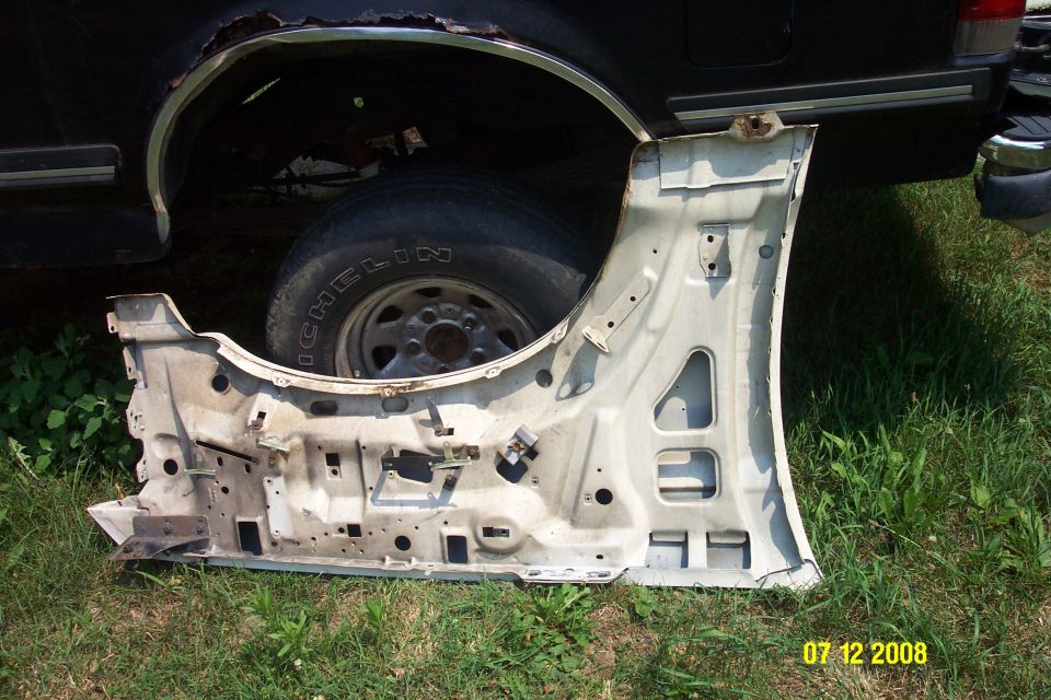 Disassembled vehicle door lying on grass next to a rusty wheel well