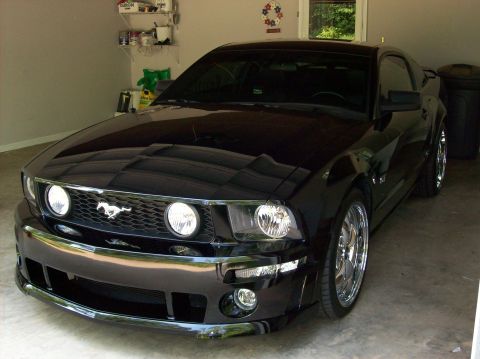 2007 Ford Mustang - A black 2007 Ford Mustang is parked in a garage, showing its distinctive grille and headlights.