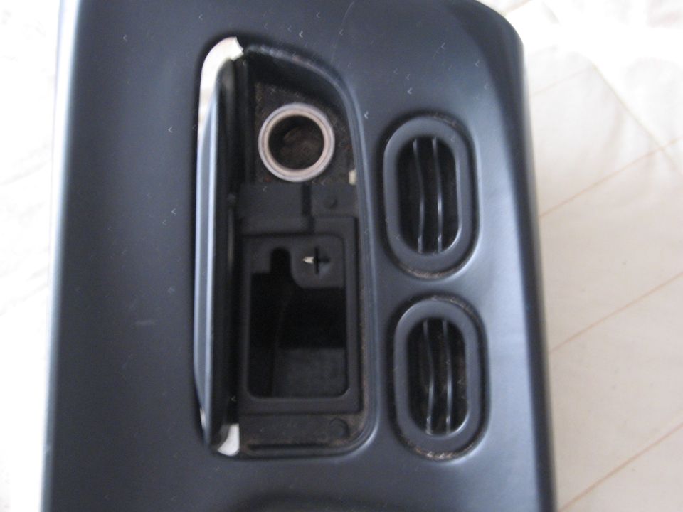 Dark gray car interior part with two oval air vents and a circular opening above a rectangular compartment