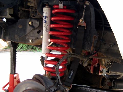 1996 Ford Bronco - Close-up view of a vehicle's front suspension system, showing a red coil spring and a shock absorber.