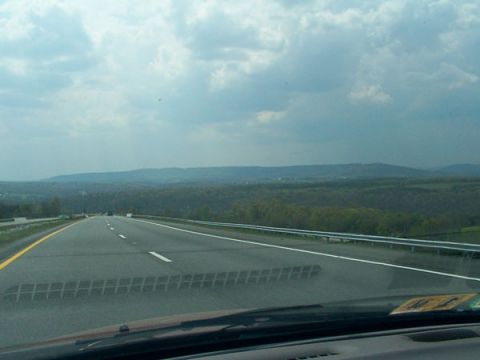 1998 Ford Taurus - A view from the driver's seat as the car travels down an open highway surrounded by a landscape of trees and hills.