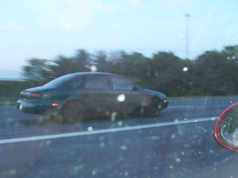 1998 Ford Taurus - A dark green sedan is captured in motion on the highway, its side profile visible against a blurred background.