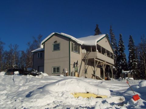 1989 Ford Bronco II - A house sits under a clear blue sky, blanketed in snow with trees surrounding it.