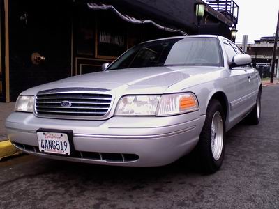 1998 Ford Crown Victoria - A 1998 Ford Crown Victoria is parked on a street in front of a building.