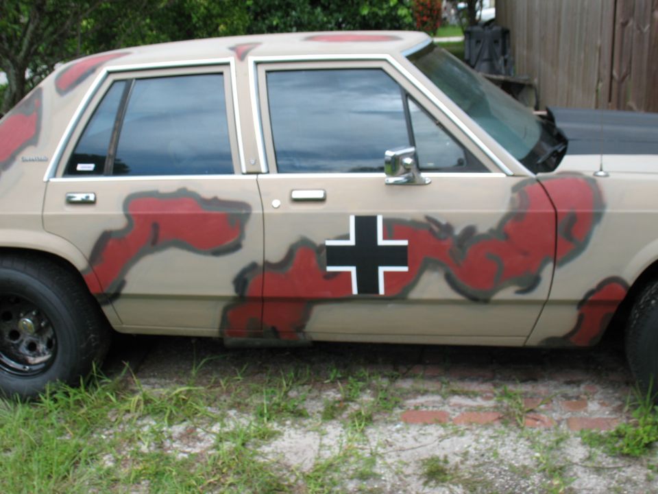 1985 Ford Crown Victoria LTD with tan, red, and black camouflage paint and a black cross emblem on the door