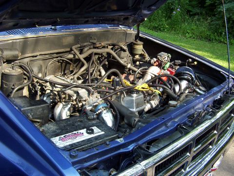 1986 Toyota Hilux - The engine bay of a blue 1986 Toyota Hilux, a modified air intake system and a prominent chrome grille.
