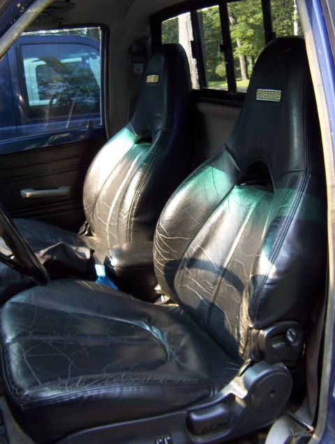1986 Toyota Hilux - Interior view of a truck's worn black leather bucket seats, with another vehicle visible through the driver's side window.