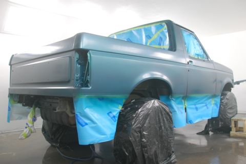 1996 Ford Bronco - A vehicle is being prepped for painting inside a booth, with protective coverings on the windows and wheels.