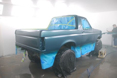 1996 Ford Bronco - A truck is being painted in a spray booth, with protective coverings on the windows and wheels.