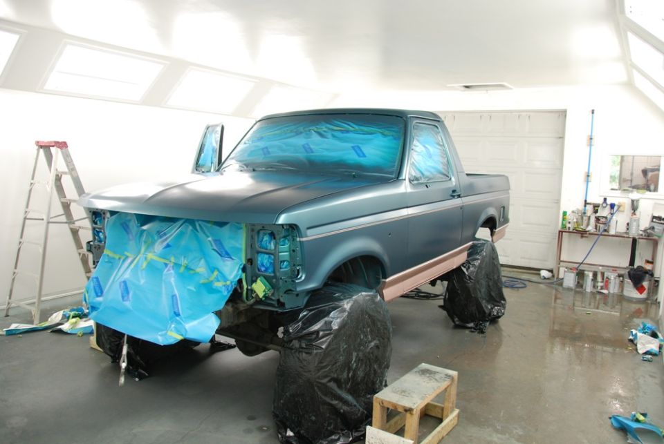 Ford truck covered in blue plastic and tape in a garage, prepped for painting. Doors are open