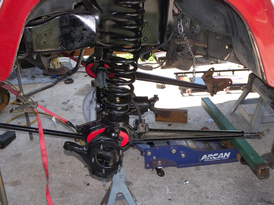 Red vehicle's front suspension assembly on jack stands, with a blue hydraulic jack