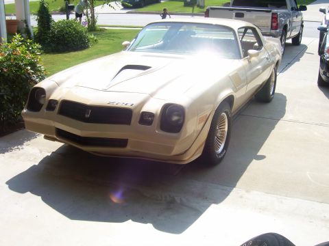 1979 Chevrolet Camaro - A tan Chevrolet Camaro Z28 is shown from the front, parked on a concrete driveway with a truck in the background.
