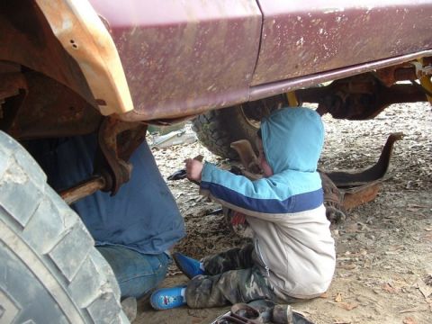 1979 Ford Bronco - A child assists with repairs underneath a vehicle, surrounded by tools and parts.