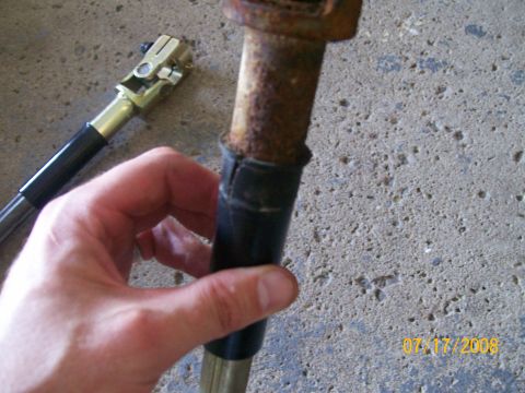 1995 Mercury Grand Marquis - A hand holds a steering shaft part, showing rust and a rubber boot. A u-joint is visible in the background.
