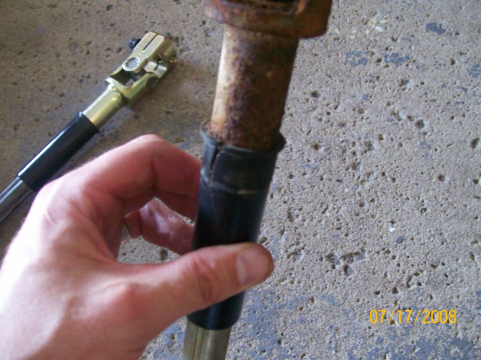Close-up of a rusty steering shaft with a rubber boot and a u-joint