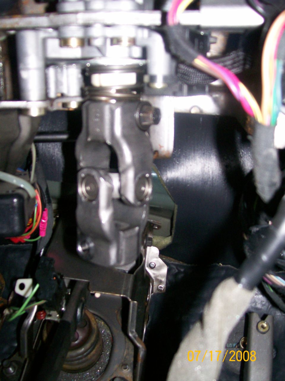 Close-up of a steering column U-joint with wires and metal brackets