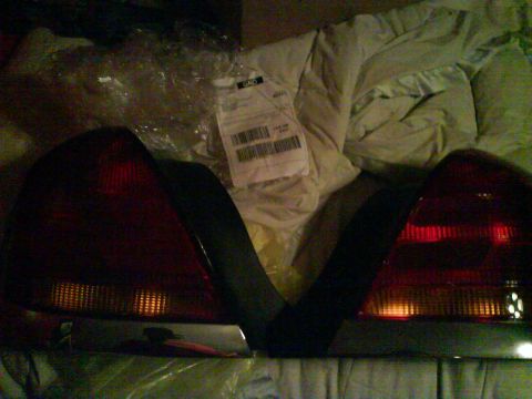 2003 Ford Crown Victoria - A pair of red and amber tail lights are shown, possibly for a Ford Crown Victoria, with a shipping label visible.