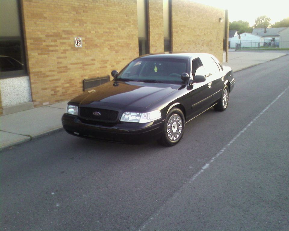Black 2004 Ford Crown Victoria parked on asphalt next to a brick building