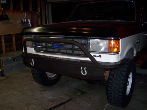 1991 Ford Bronco - Front view of a Ford Bronco with a custom bumper and tow hooks, parked indoors.