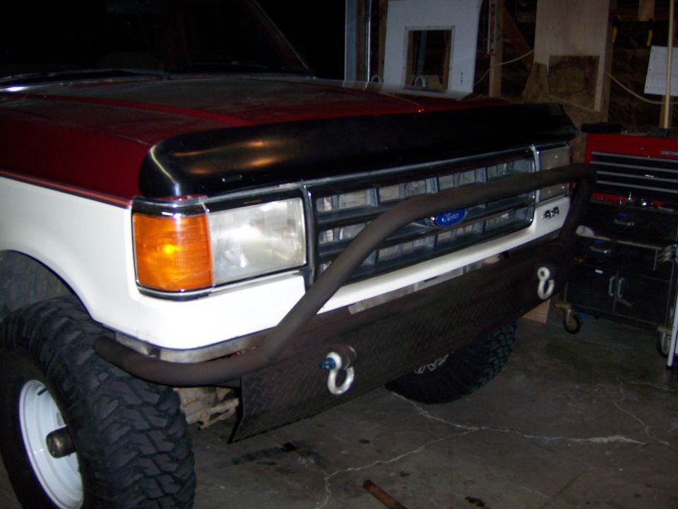 Custom diamond plate bumper with tow hooks on a red and white truck