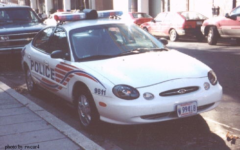 1998 Ford Taurus police car parked on street, with other cars in background