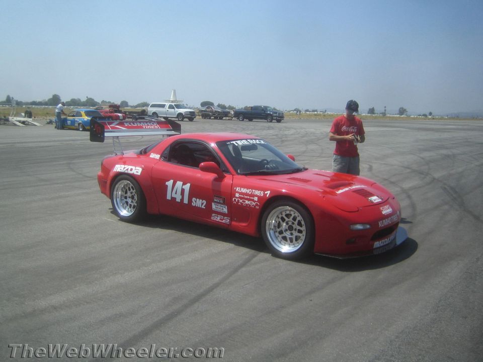 Red Mazda RX-7 race car with large rear wing and number 141 on door, parked on asphalt