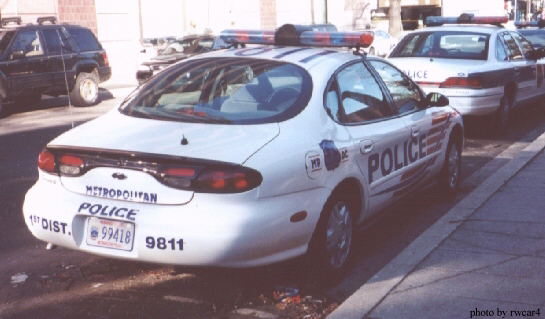 Police car with 'METROPOLITAN POLICE' on trunk, license plate 99418 9811. Another police car is behind it