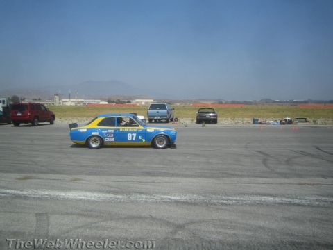 1985 Ford Mustang - A blue and yellow race car with the number 97 is seen on a track, with other vehicles in the background.