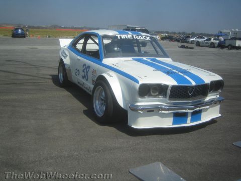 1985 Ford Mustang - A Mazda race car with "Tire Rack" branding is parked on an asphalt surface, possibly a track.