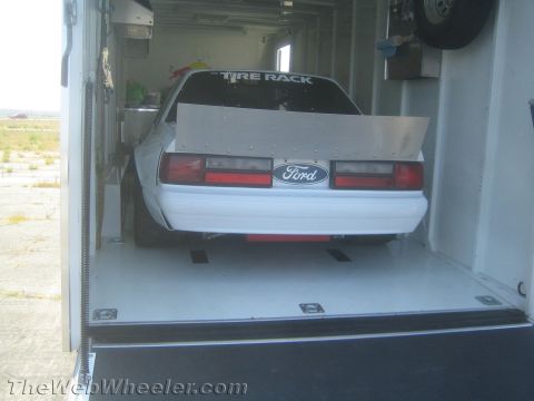 1985 Ford Mustang - A white 1985 Ford Mustang race car is being transported in a trailer, ready for the track.