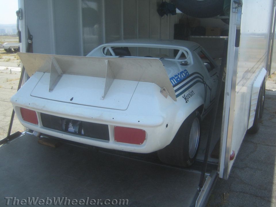 White Mazda race car with large rear spoiler and Hoosier tires being loaded into a trailer