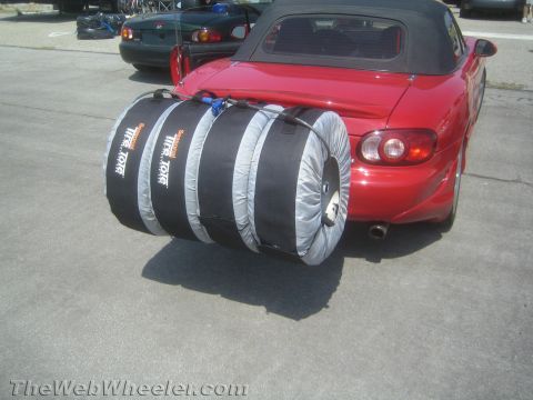 1985 Ford Mustang - A red convertible is parked outdoors, with a large tire tote mounted on its rear bumper.