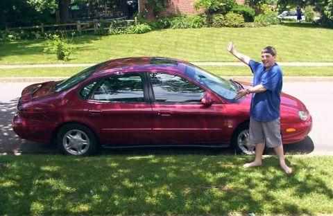 1998 Ford Taurus - A red 1998 Ford Taurus is parked on the side of the road with a person standing next to it.