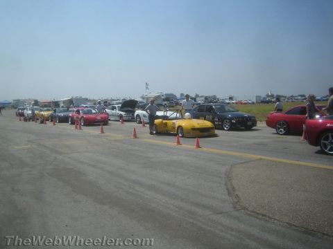 1985 Ford Mustang - Several cars are lined up on a race track, with a yellow convertible in the foreground.