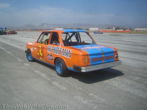 1985 Ford Mustang - A modified car with racing decals sits on a paved surface, possibly a racetrack, under a clear sky.