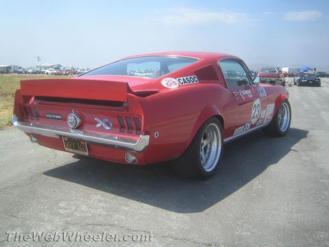1985 Ford Mustang - A red 1967-1968 Ford Mustang fastback, modified for racing, is seen from the rear on a sunny day with other vehicles in the background.