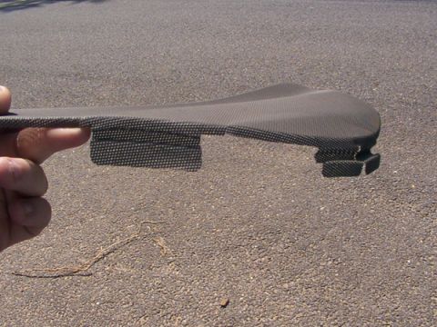 1998 Ford Taurus - A hand holds a carbon fiber trim piece against a gravelly background.