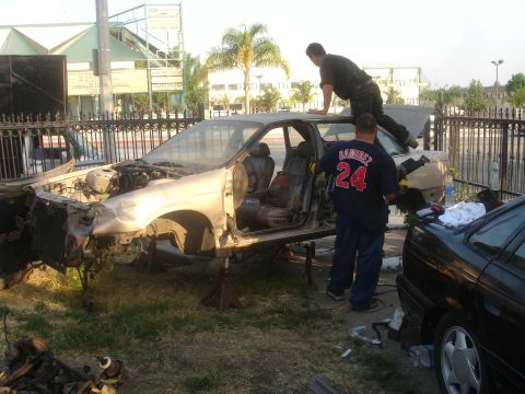 1991 Ford Taurus - A car is being dismantled outdoors with two people actively working on it.
