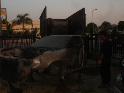 1991 Ford Taurus - A heavily damaged sedan is being worked on outdoors, with a man observing the vehicle.