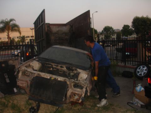 1991 Ford Taurus - Two men load a heavily damaged car onto a truck bed at dusk.