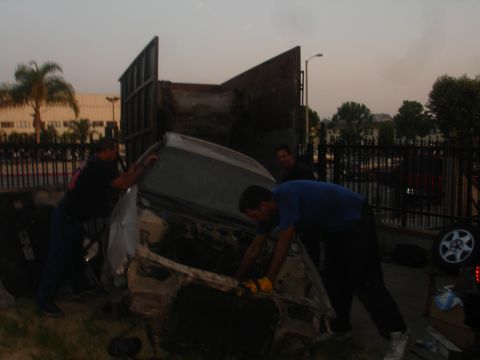1991 Ford Taurus - People are loading a damaged car into the back of a large truck.