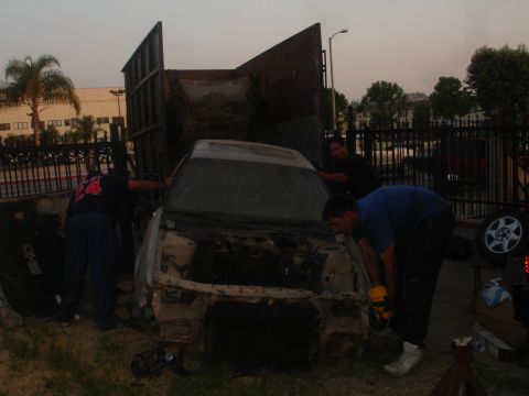 1991 Ford Taurus - Men work on a car being loaded into a truck, its front end is dismantled.