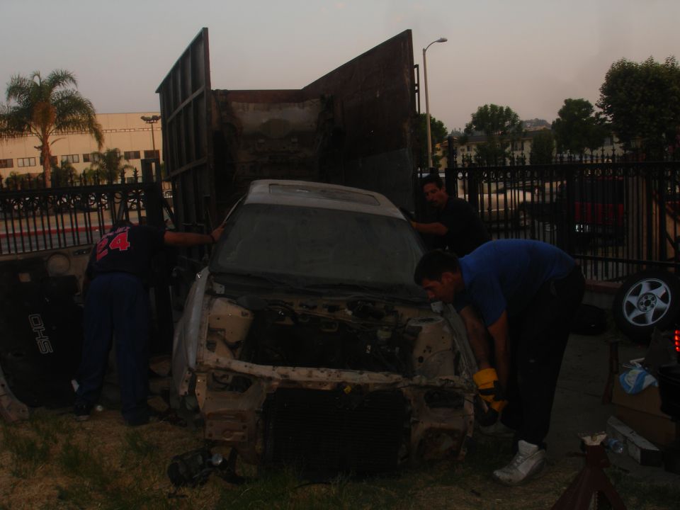 Car being loaded into a truck, front end removed, men working