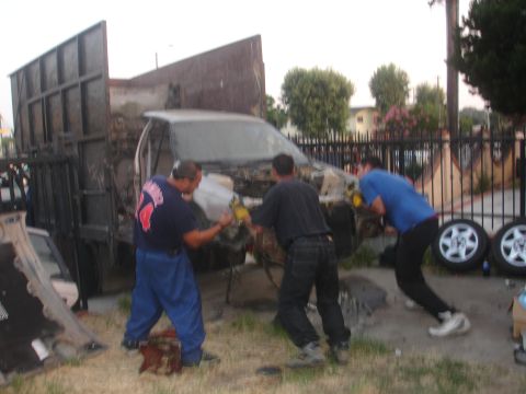 1991 Ford Taurus - A group of men are actively dismantling a damaged vehicle, possibly for scrap or parts.