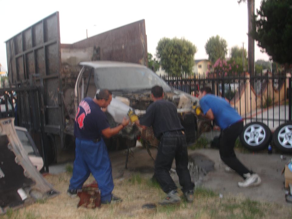 Three guys are working on a wrecked car that's being loaded into a truck bed